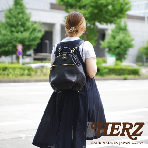 黑色皮革後背包，附有金色拉鍊和鎖扣，背包底部有四個金色腳釘。