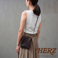 職人手作深棕色皮革Organ迷你杜勒斯側背包，帶有金屬扣環，斜背於身穿白色蕾絲上衣和米色長裙的女性身上。