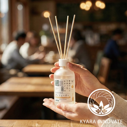 KYARA INNOVATE 室內擴香竹，手持玻璃瓶，瓶身標有「DIFFUSER」與「SCENT APPLE CIDRE」字樣，數根擴香枝插入瓶中，背景為模糊的室內用餐場景