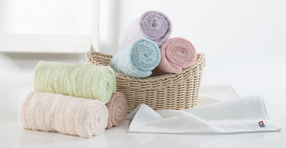 一籃子捲起來的淡紫色、淺藍色和粉紅色毛巾，旁邊疊著兩條淺綠色和淺粉紅色的毛巾，還有一條展開的白色毛巾