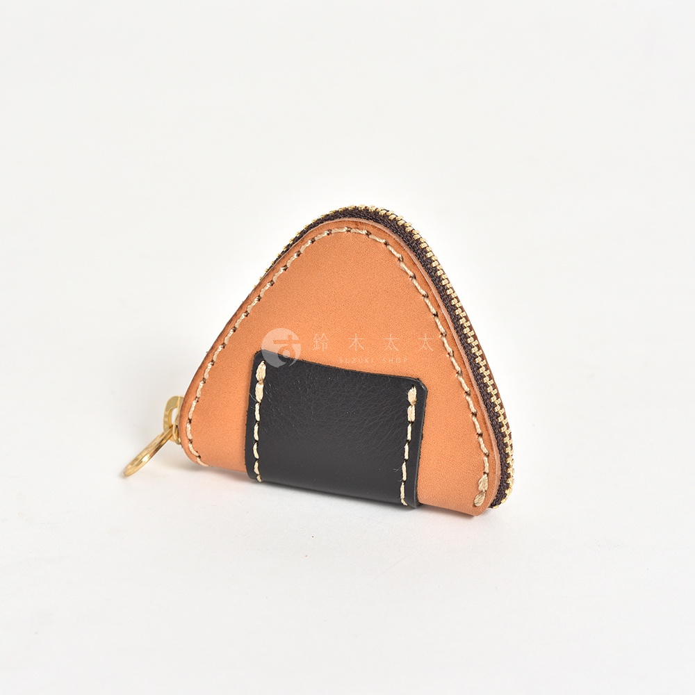 這是一款造型獨特的職人手作皮革三角飯糰零錢包，主體採用棕褐色Latigo皮革製成，底部拼接一塊黑色皮革模擬海苔外觀，並配有細緻的淺色縫線與黃銅色拉鍊，整體呈現可愛精緻的手工質感。