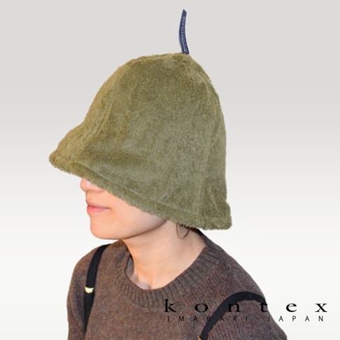 一位女士戴著橄欖綠色的毛巾布桑拿帽，帽子材質柔軟，帽簷較寬，頂部有一個藍色標籤。