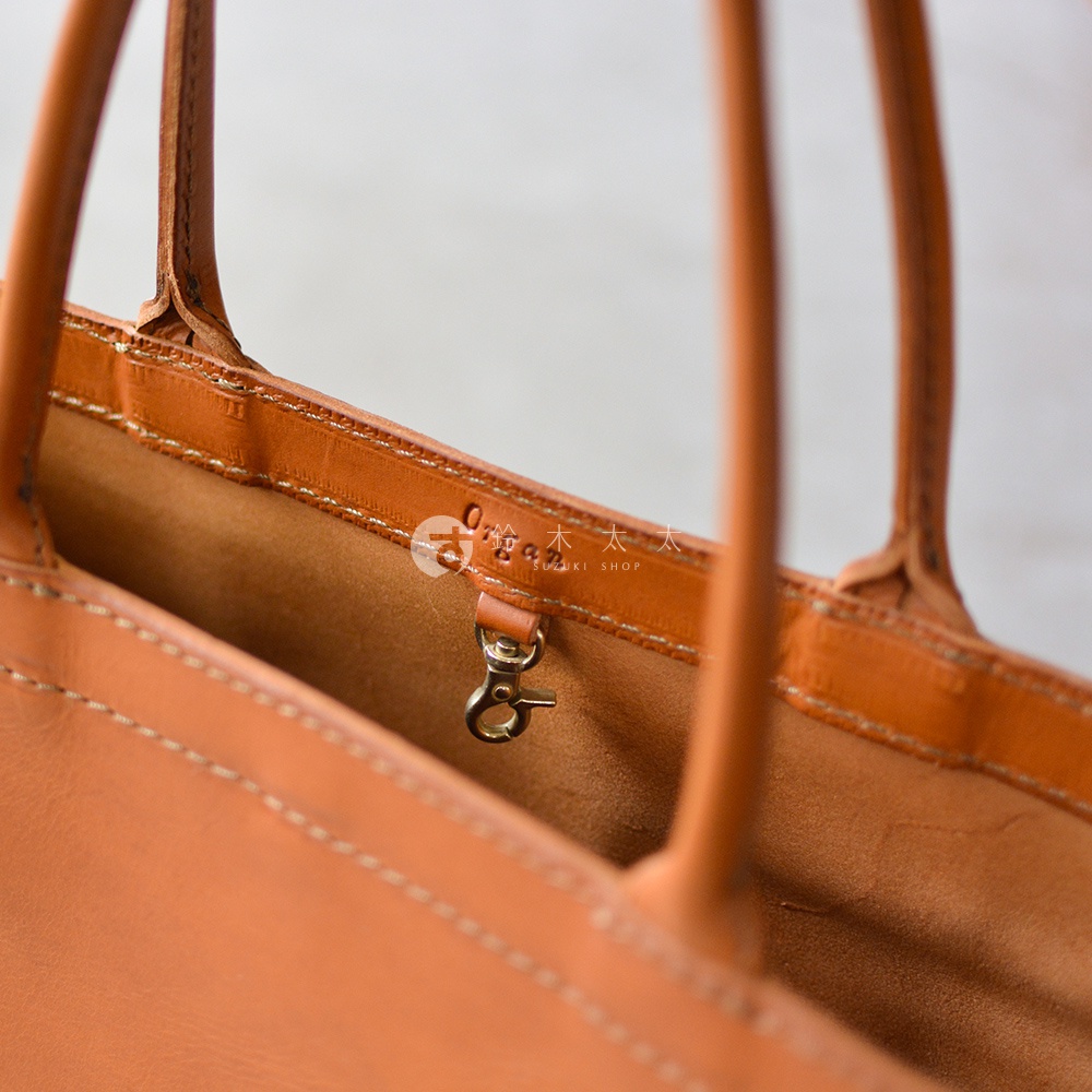 近距離拍攝，展示了橙色皮革托特包的內部細節，包括縫線、皮革手柄和一個金屬掛鉤。
