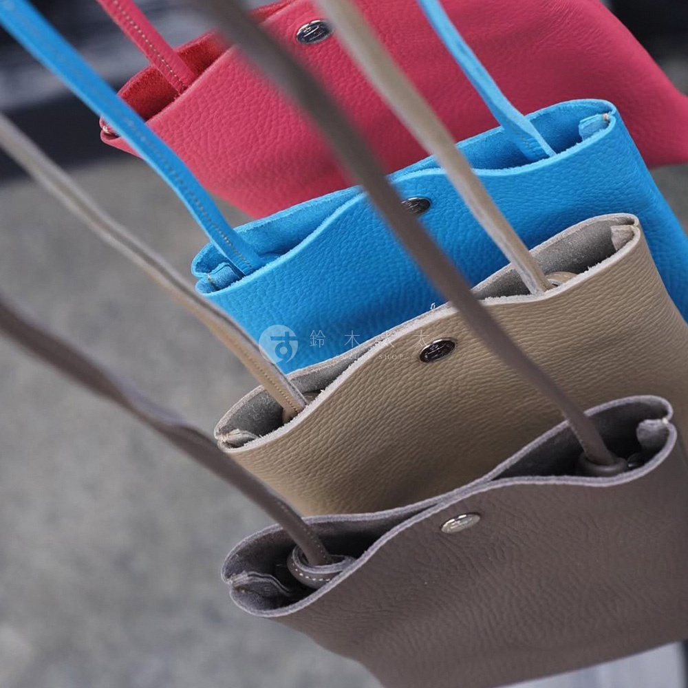 四個皮革手機包，顏色由上至下分別為桃紅、亮藍、淺棕和深棕，皆配有細長肩帶，包身呈現柔軟的垂墜感，並飾有金屬按扣。