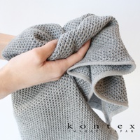 手持一條灰色鬆餅紋棉麻混紡毛巾，材質柔軟，紋理細緻，邊緣有淺灰色滾邊。