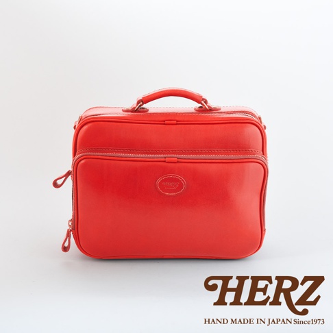 紅色皮革製作的職人手作兩用商務公事包，有雙提把、前後拉鍊口袋，正面中央有品牌壓印標誌。
