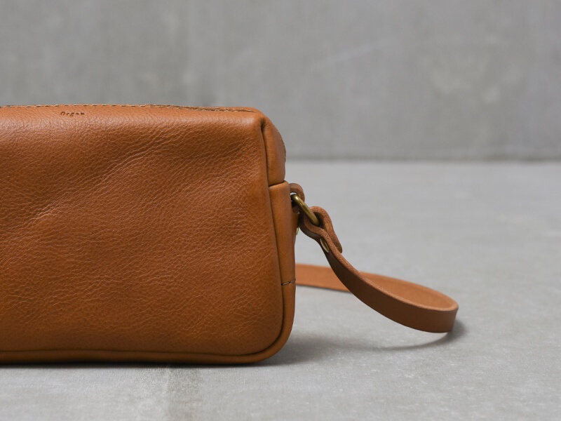 職人手作皮革Organ輕巧拉鍊單肩包 (G-80) S，採用棕色皮革製成，質感細膩，帶有品牌壓印。包款一側有可拆卸的皮革提把，透過金屬環連接。