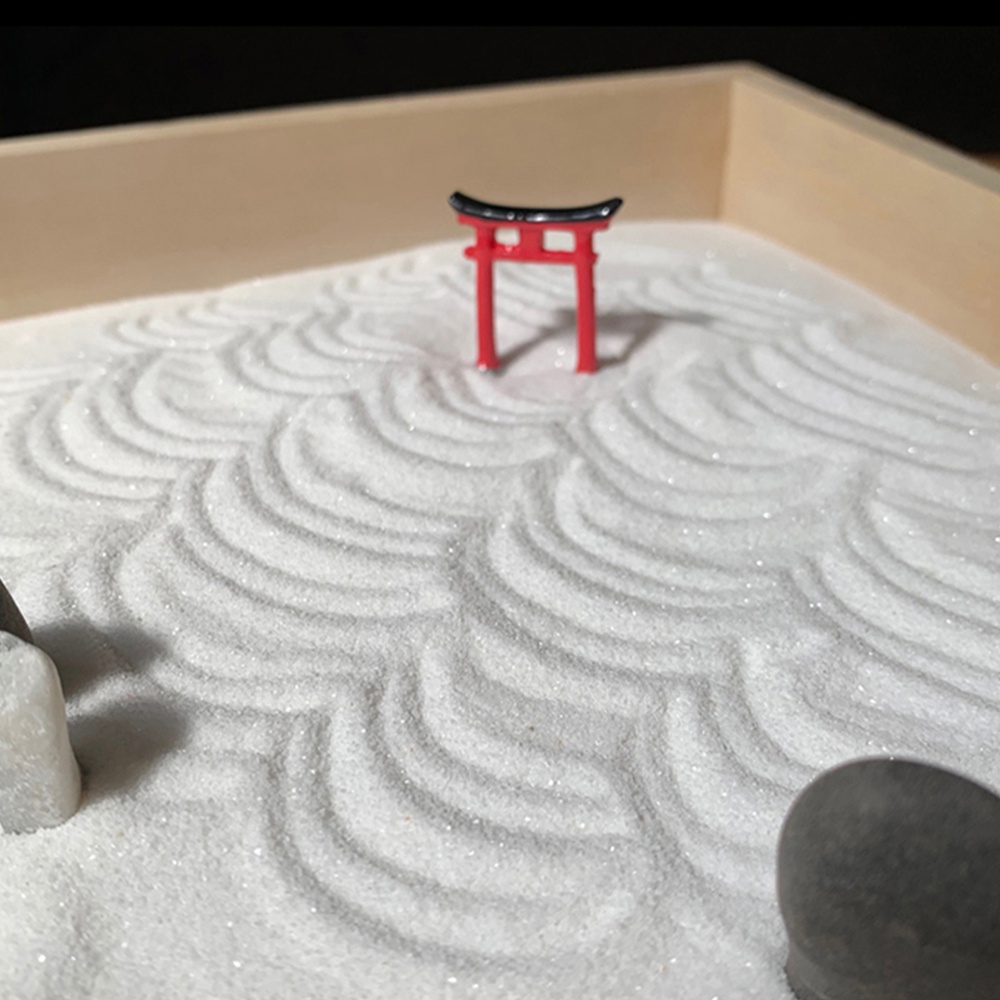 迷你枯山水模型，以白色細砂為底，砂上耙出波浪紋理，中央立著一座鮮紅色的鳥居，頂部為黑色屋簷，旁邊置有兩塊素色石頭，整體置於淺木色淺盤中。