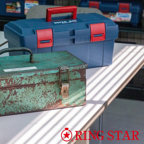 藍色塑膠雙層工具箱，配有紅色提把和紅色鎖扣。前方一個綠色金屬工具箱，表面有明顯的舊化和刮痕，配有金屬提把和鎖扣。