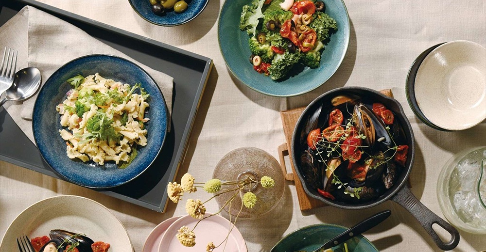 多個裝有美味料理的盤子和碗，擺放在米白色的桌布上。