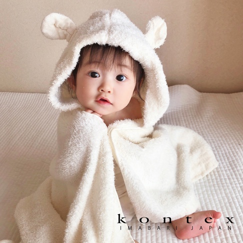 一名嬰兒裹著一件厚實、柔軟的白色連帽浴巾，浴巾上有可愛的兔耳朵設計。