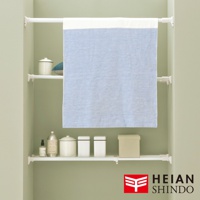 白色伸縮桿層架，附有兩個白色層板，層板上擺放著白色收納罐、乳液瓶和一個米色收納盒。上方掛著一塊藍白相間的布。