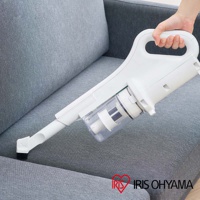 白色手持充電吸塵器，配備透明集塵筒和毛刷吸頭，正在清潔灰色布藝沙發。