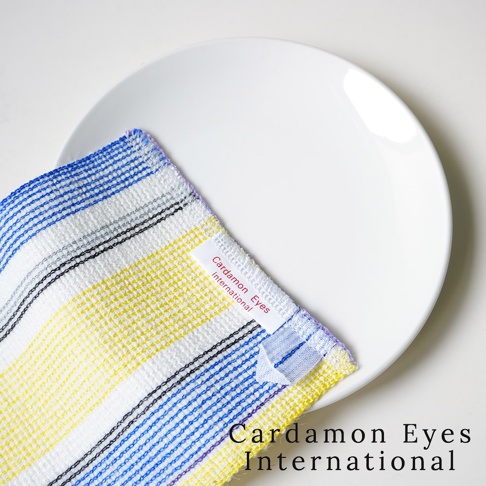 一塊橘黃色、藍色、灰色和紫色條紋的壓克力纖維清潔巾，上面有「Cardamon Eyes International」的標籤，放在白色盤子上。