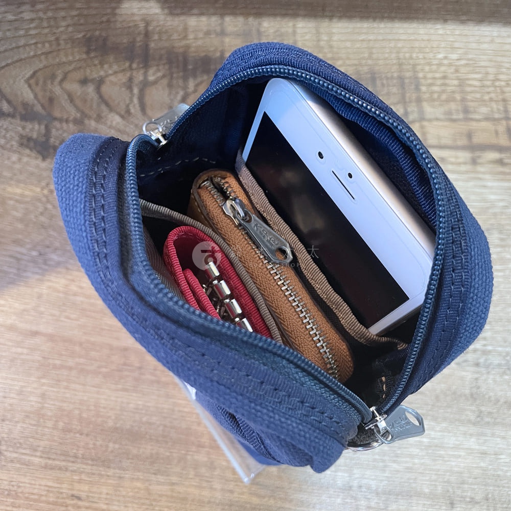 深藍色石洗帆布斜背手機包，內部裝有白色手機、棕色皮質零錢包及紅色鑰匙圈。