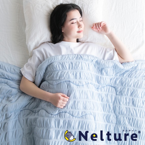 淺藍色單人被，表面有細緻的壓紋與縫線，呈現波浪狀紋理，觸感輕柔，一位女子蓋著被子安詳入睡。