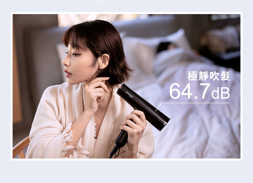 一位女性手持黑色吹風機，背景是床鋪，吹風機上顯示極靜吹髮 64.7dB。