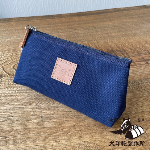 石洗帆布製成的小型收納包，深藍色，帶有皮革飾牌和拉鍊開合。