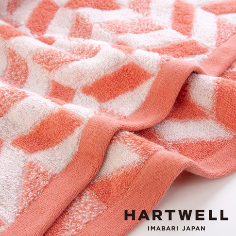 今治和風傳統紋樣言織浴巾，珊瑚橘與白色織紋交織，展現幾何圖案，材質柔軟，觸感細緻。