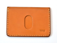 職人手作皮革橫式票券收納夾 (KC-36)，採用光滑的棕褐色皮革製成，正面中央有一個垂直的橢圓形開口。側邊和底部有明顯的米色縫線，右下方壓印有「HERZ MADE IN JAPAN」字樣。