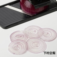 黑色塑膠製的四合一刨絲器，刨出數片紫洋蔥圈，呈現同心圓紋理。