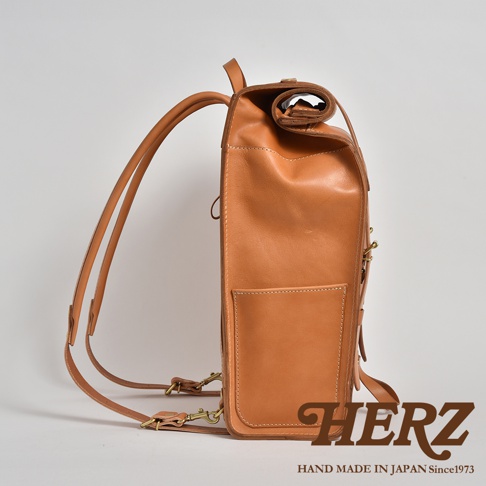 棕色皮革後背包，側邊視角，皮革材質，配有可調整的肩帶和金屬扣環，包身有外層口袋，頂部採捲口設計。