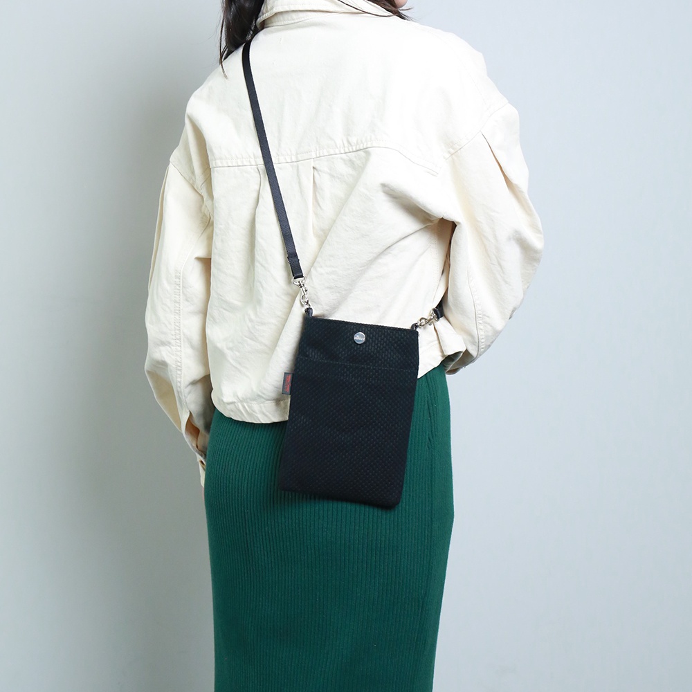 黑色三河木綿刺子織手機包，附有細長黑色背帶，可斜肩配戴。包身有立體紋理，頂部有金屬按扣。