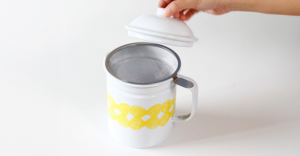 白色琺瑯濾油壺，壺身飾有黃色編織紋路，配有金屬濾網和白色壺蓋。