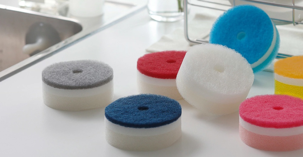 多種顏色圓形洗碗海綿，帶有白色底部層和彩色頂部層，放置在廚房檯面上。