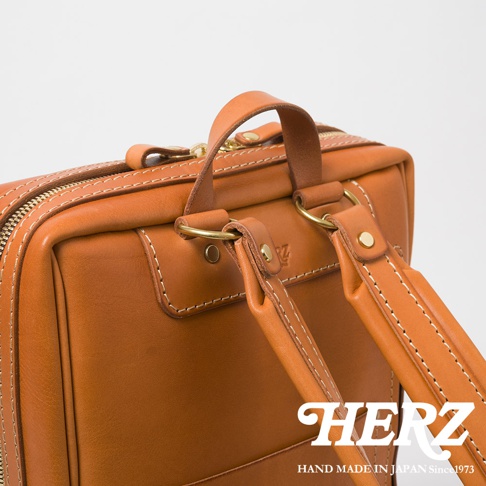 職人手作皮革軟皮商務後背包 R-28，展示駝色皮革的紋理與精緻縫線，設有頂部提把與可調節的皮革雙肩帶，搭配黃銅色五金配件。