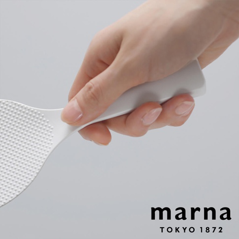 marna TOKYO 1872 品牌標誌旁，一只手正握著白色站立式飯匙，飯匙表面佈滿細小的圓點紋路。