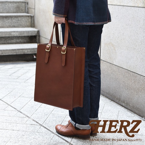 職人手作皮革商務用紙袋托特包，經典方形設計，採用堅韌的棕色皮革，配有金色金屬扣環和雙提把，適合日常商務使用。