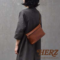 一名女性身穿深灰色長袍，側身展示一個棕色皮革斜背包，包包橫跨在胸前。