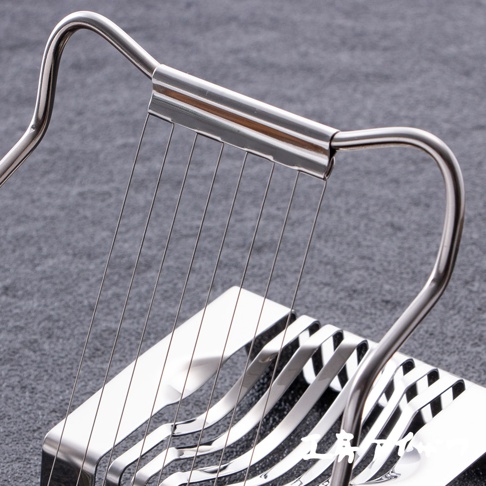 銀色不鏽鋼材質的切蛋器，帶有弧形握把和多條細長的切割線，置於灰色背景上。