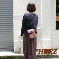 一位女士背著一個棕色皮革製成的斜背包，包包上有金屬扣環和縫線細節。