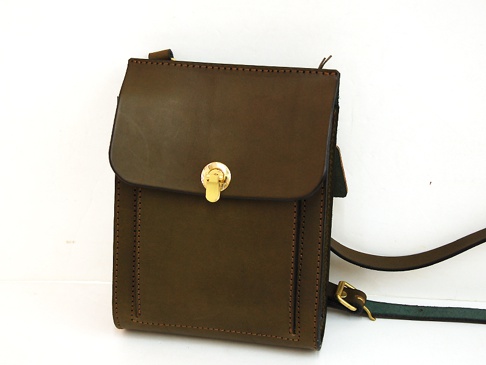 深棕色厚實皮革製成的手提斜背包，正面有翻蓋設計，配有金色旋轉鎖扣，包身縫線清晰，附有可調節的皮革背帶。