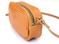 淺棕色皮革製成的手工隨身單肩小包，具有金屬拉鍊和可調節的皮革背帶，透過縫線裝飾。