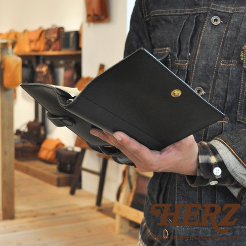 職人手作皮革手帳/記事本書套，黑色，附有金屬按扣，皮革材質，展示於店內背景。