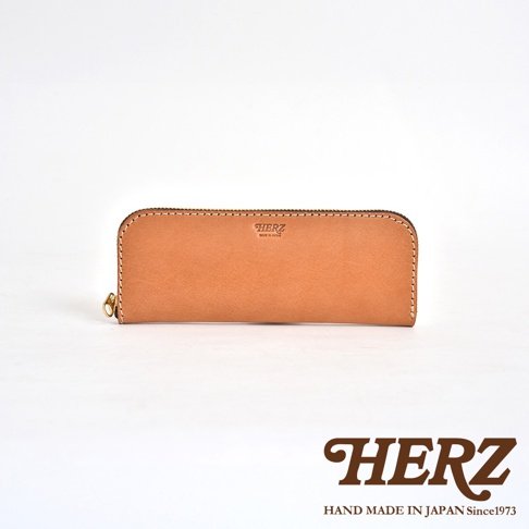 一個 tan 色皮革長形拉鍊筆袋，表面有一個燙印的 HERZ 標誌和 MADE IN JAPAN 字樣。