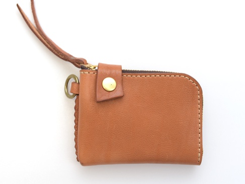 棕色皮革製成的拉鍊短夾，帶有金色金屬拉鍊、皮革提帶和鑰匙圈。側面有編織細節和白色縫線。