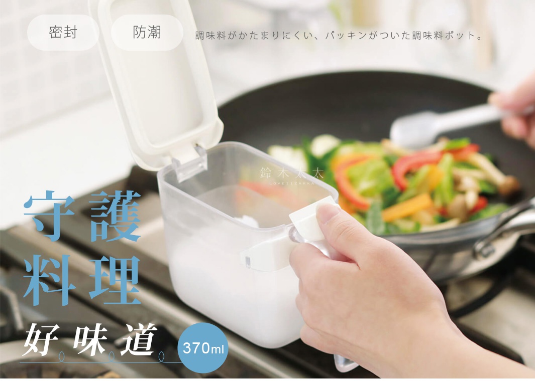 手持透明調味料盒的特寫，蓋子上方標註密封與防潮，盒身容量為370毫升。背景為正在烹飪蔬菜的炒鍋，調味盒設計簡潔，握把方便操作，展現廚房居家用品的使用場景。