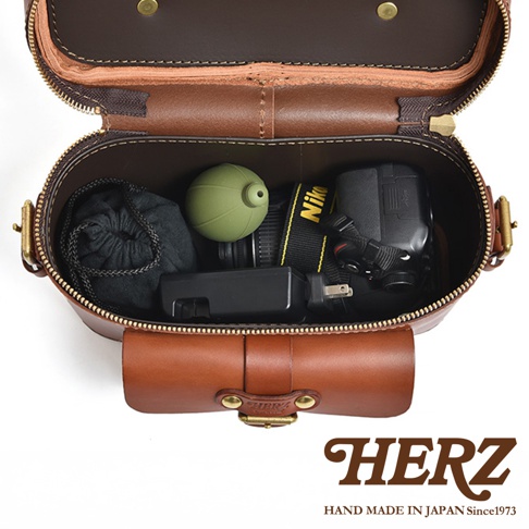 日本HERZ職人手作皮革厚實相機包 N-8，打開的棕色皮革包內裝有綠色鏡頭蓋、Nikon相機及黑色收納袋，下方有HERZ品牌標誌及 HAND MADE IN JAPAN Since1973 字樣。