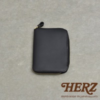 黑色皮革拉鍊式記事本收納包，附有金色拉鍊和皮革拉環，背景為灰色紋理表面。