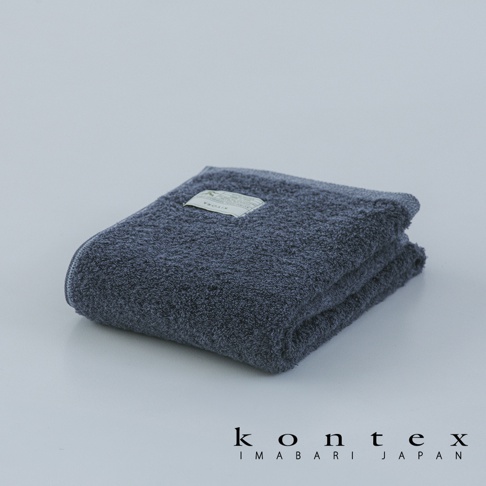 這是一張摺疊平放在淺色背景上的 KONTEX 品牌深藍色毛巾，毛巾表面擁有厚實的纖維質感，中央繡有該品牌的 KIYORA 系列專屬標籤，底部則呈現 Kontex Imabari Japan 的品牌標誌。
