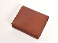 職人手作皮革直式卡片收納雙折短夾，採用溫潤的棕色皮革，以手工縫線精緻車縫，展現簡約的雙折設計與金屬拉鍊細節。