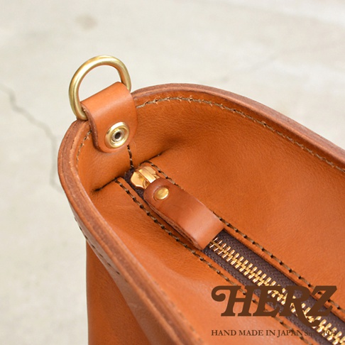 日本 HERZ 職人手作皮革托特包的頂部視角，特寫金屬 D 型環、拉鍊及縫線細節。