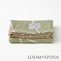 一條疊好的淺綠色純棉浴巾，帶有米色和白色的幾何線條圖案，上面有一個標籤。