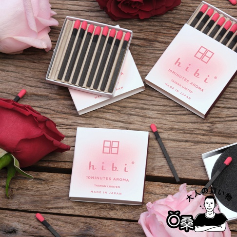 香氛火柴組合台灣限定版，內含三盒火柴，每盒均為白色印刷，印有「hibi」品牌標誌、10MINUTES AROMA、TAIWAN LIMITED字樣，以及「MADE IN JAPAN」產地標示。火柴棒為黑色，頂端有粉紅色火柴頭，擺放在木質桌面上，周圍有粉紅色和紅色玫瑰花瓣裝飾。