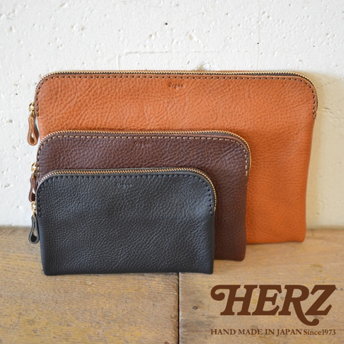 三款職人手作Organ雙拉鍊收納袋，由皮革製成，分別為橘棕色、深棕色及黑色，帶有金色拉鍊，展現質感。