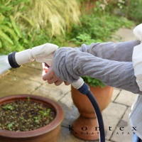 淺灰色棉麻混紡彈性袖套，織紋明顯，雙臂皆配戴，展示於戶外庭園，手持白色水管噴嘴。